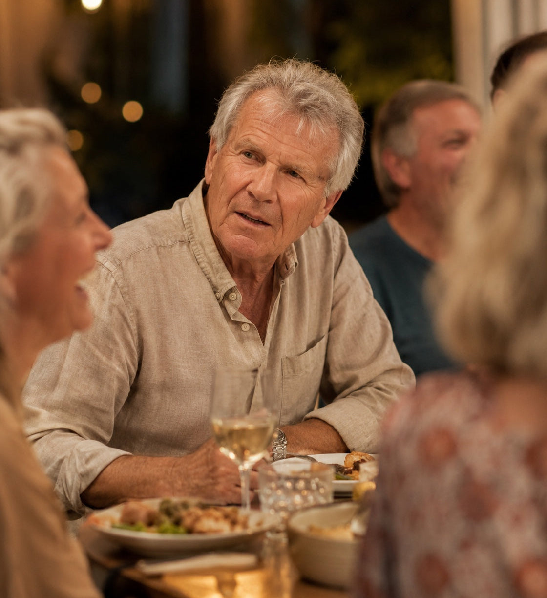 Man sitting at a dinner table with others, engaged in conversation.